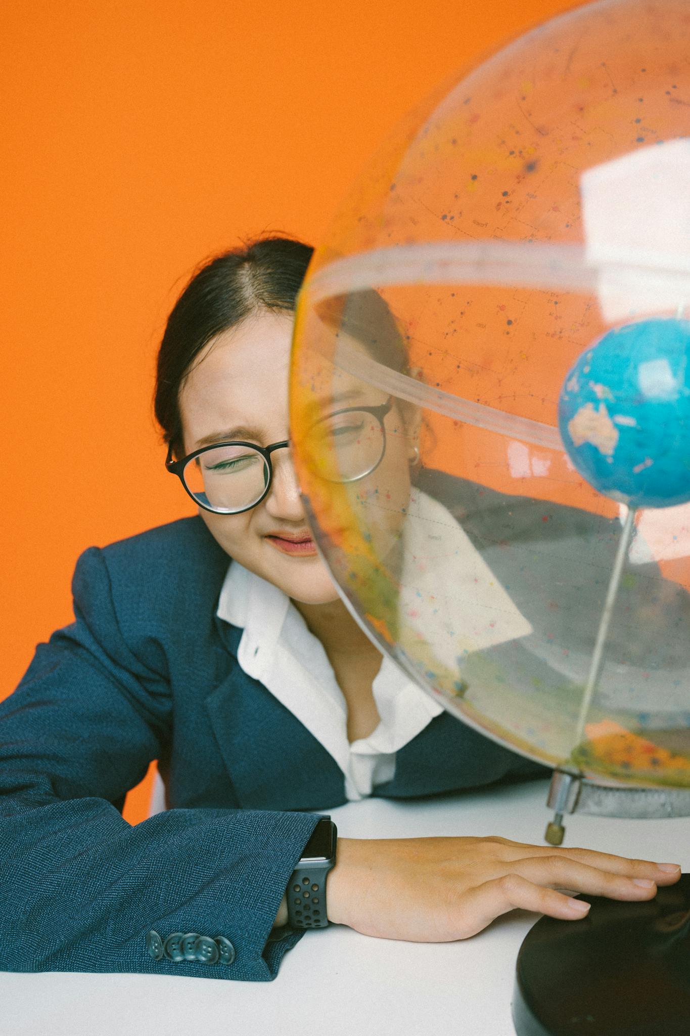 Asian businesswoman in glasses with globe against orange background, symbolizing global business and education.