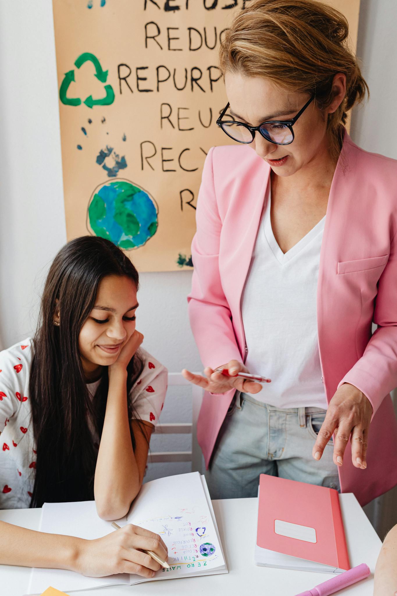 Female teacher assisting teenage girl with homework in classroom setting.